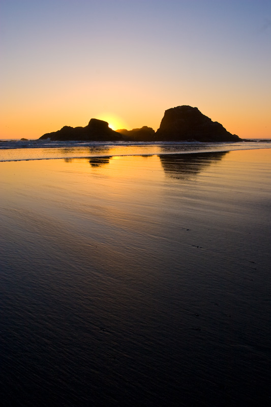 Seastack Silhouettes Reflected In Wet Sand At Sunset